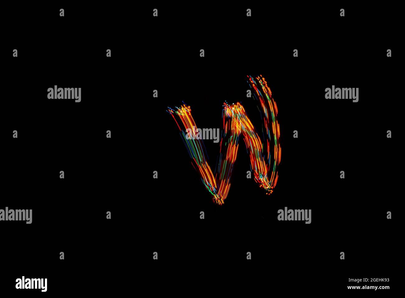 Letter W. Light painting alphabet. Long exposure photography. Drawing letter W with colorful lights on black background. Stock Photo