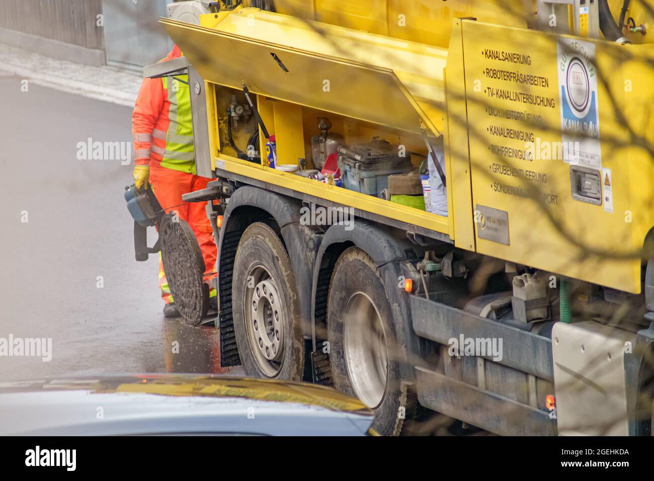 Maintenance at a manhole with a unrecognizable man, working behind the sewer cleaning vehicle on the open street. Stock Photo