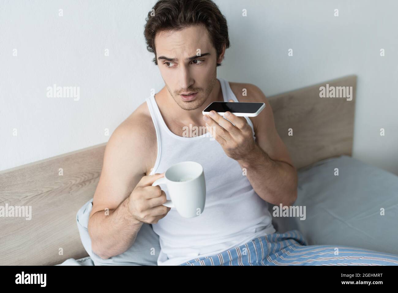 young man sending voice message while holding cup of coffee Stock Photo