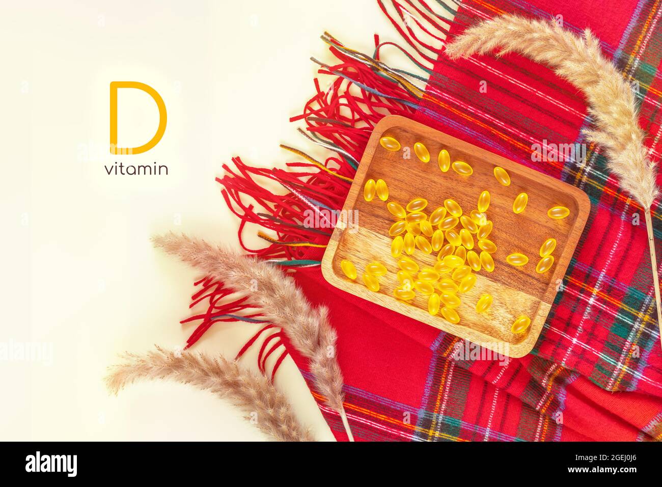 Horizontal banner with vitamin d teme. Autumn composition with wooden plate with yellow vitamin gel capsules, red cashmere palatine and dried flowers Stock Photo