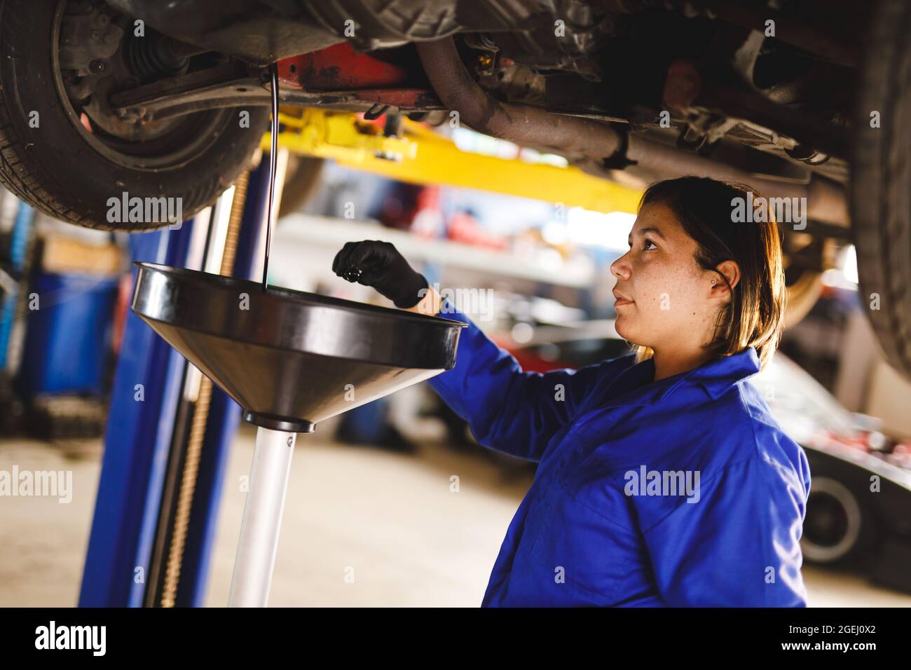 Mixed race female car mechanic wearing overalls, checking oil