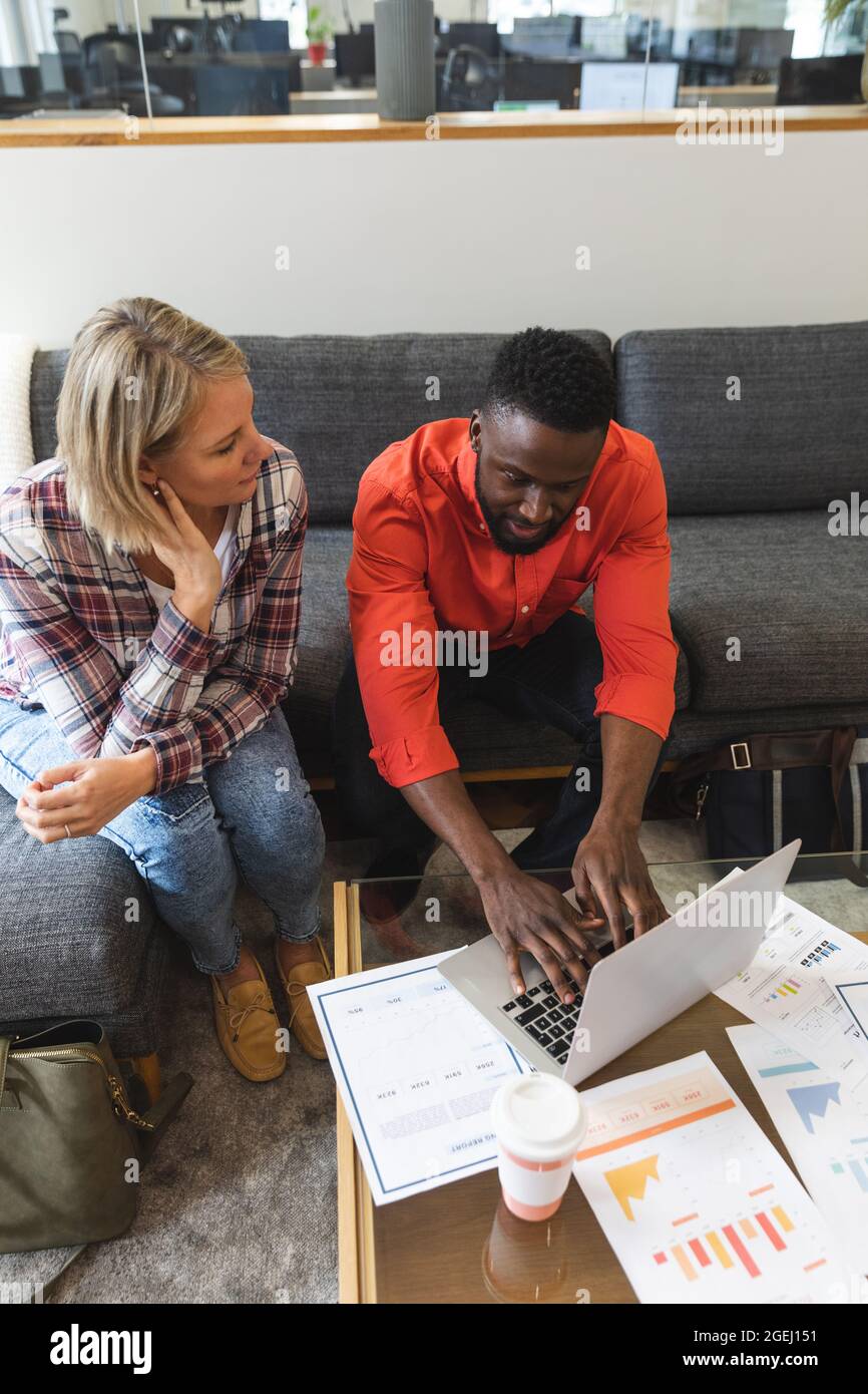 Smiling diverse female and male colleagues sitting on sofa at workplace ...