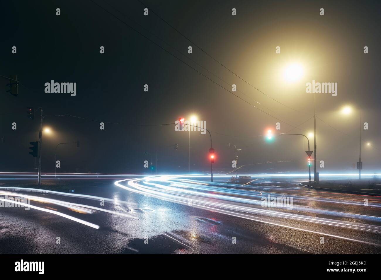 Light trail of cars passing crossroad at foggy night. Stock Photo