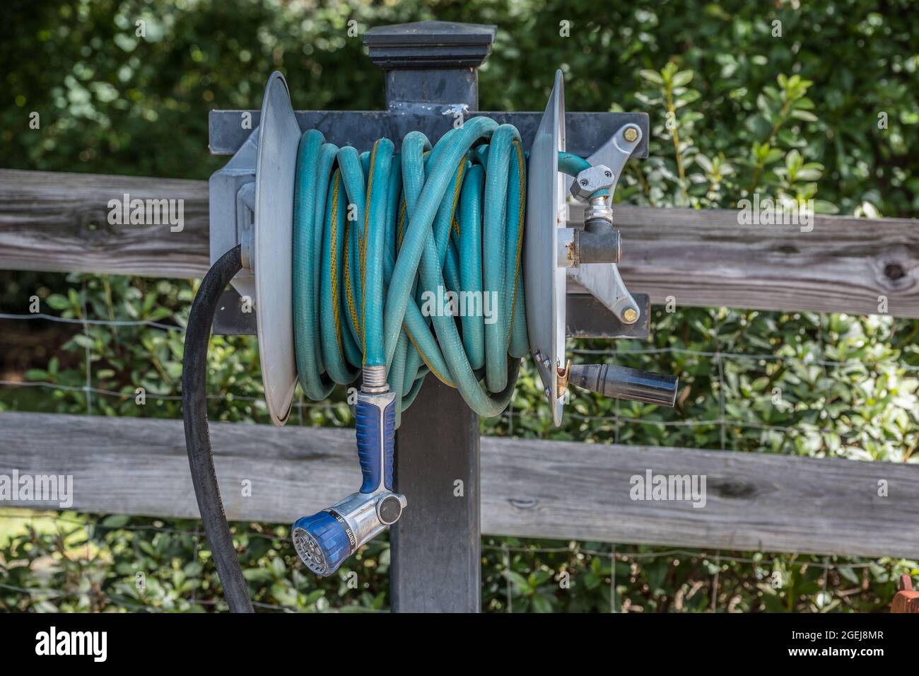 Heavy duty gardening hose with a hand sprayer attached coiled up on a metal  reel that