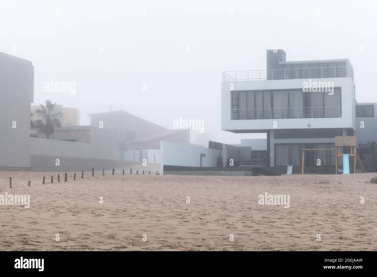 Exterior of a white and grey modern villa on ocean coast in high-end, luxury housing development on a foggy day on beach. Architecture background Stock Photo