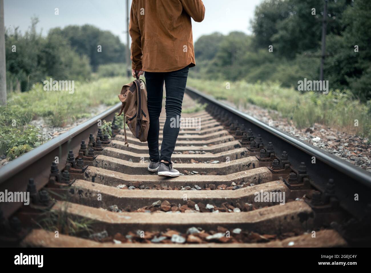 Hipster teen in black jeans pants and grey sneakers with backpack on railway. Travel concept Stock Photo