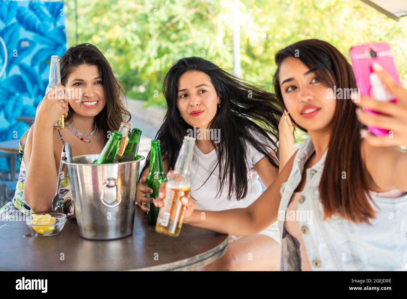 Three young latin friends having their picture taken while drinking beers. Girl friends enjoying a nice summer evening on a terrace. Girl friends taki Stock Photo