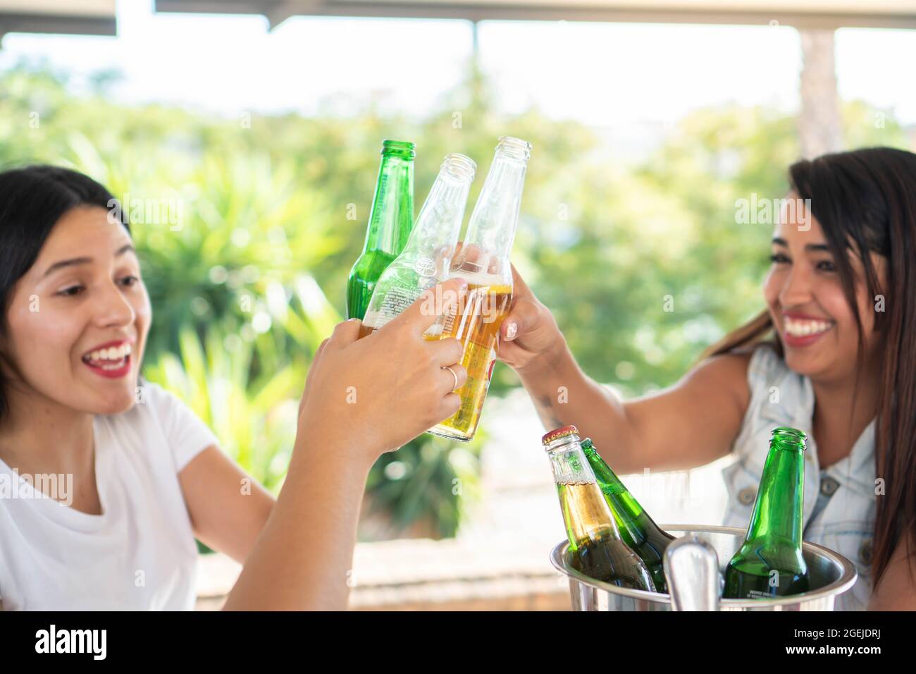 Three young latin girl friends making a toast with their beers. Hispanic friends having drinks in good company. Smiling girls toasting in a bar on a s Stock Photo