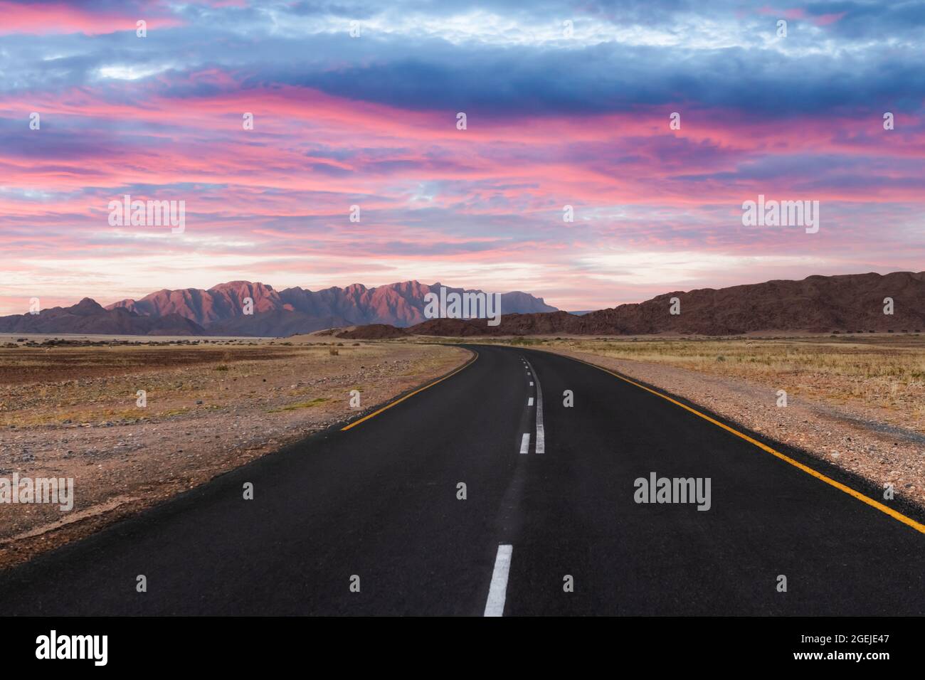 Asphalt road through desert savanna in of Namib at Namib-Naukluft National Park in Namibia, Africa. Highway and sunset sky Stock Photo