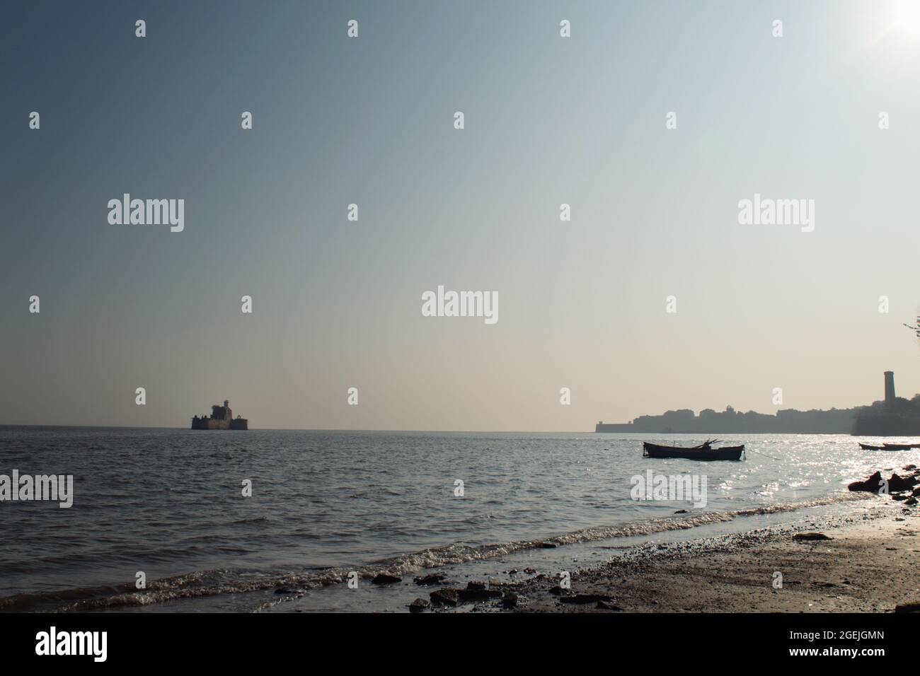 View of the Arabian sea from a sandy beach. Silhouette of the boat, the Lighthouse and the City are visible on the bright sunny day, Diu, India. Stock Photo