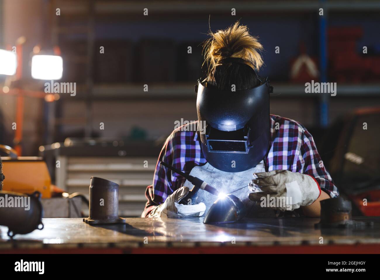 Mixed race female car mechanic welding car part in Stock Photo