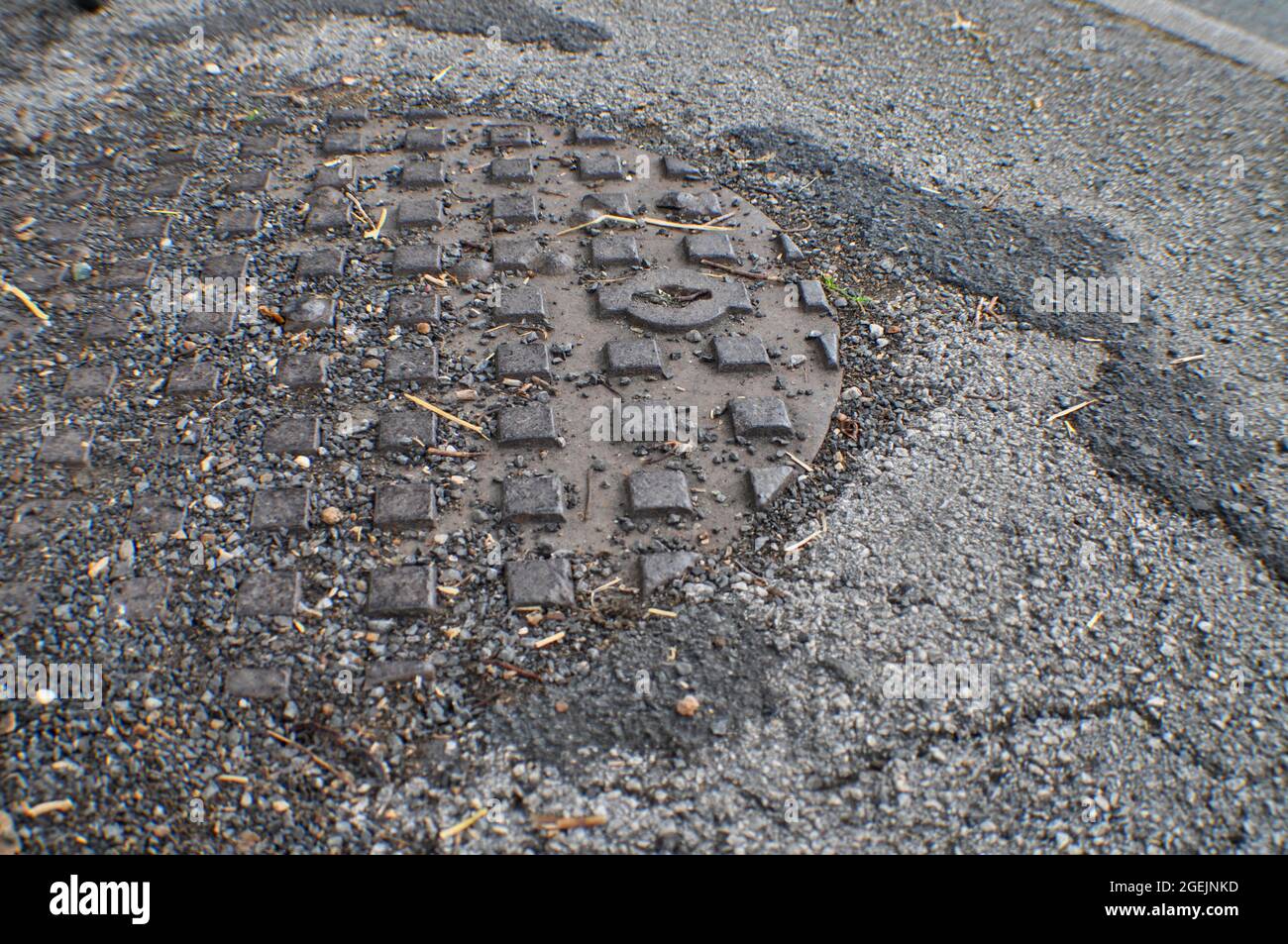 Man hole cover partly covered with stones and loose tarmac chippings Stock Photo