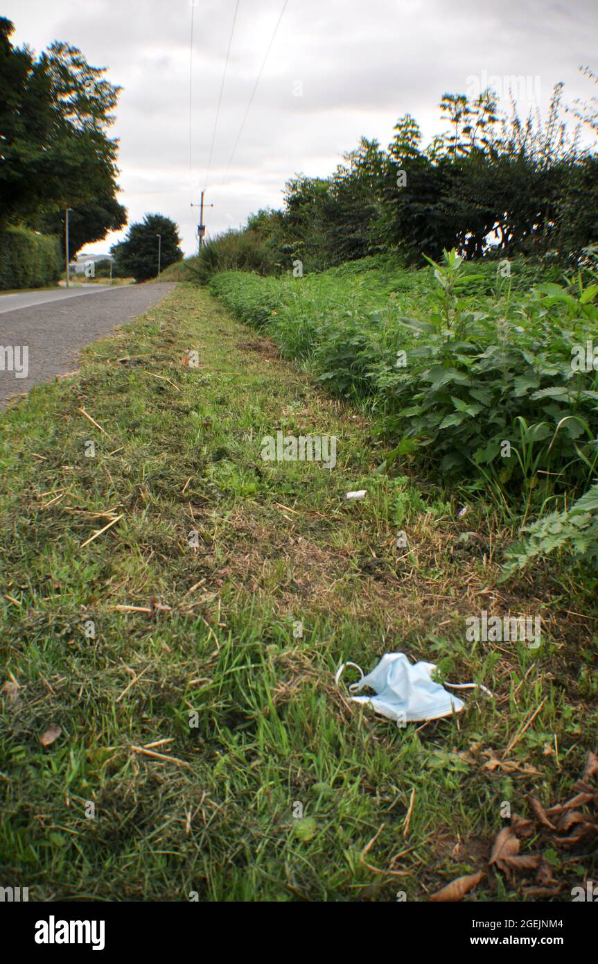 A discarded disposable face mask in the grass verge along a country road  on the edge of a village Stock Photo