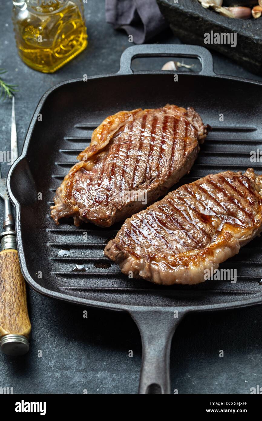 Fried strip loin steak on cast iron grill pan with olive oil and rosemary,  black background Stock Photo - Alamy