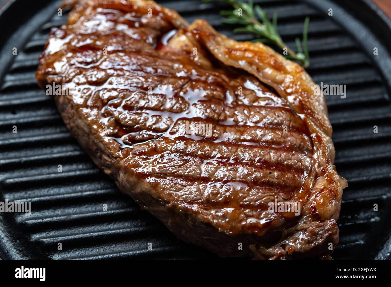 Fried strip loin steak on vintage cast iron grill pan and cutlery set, black background. Top view Stock Photo
