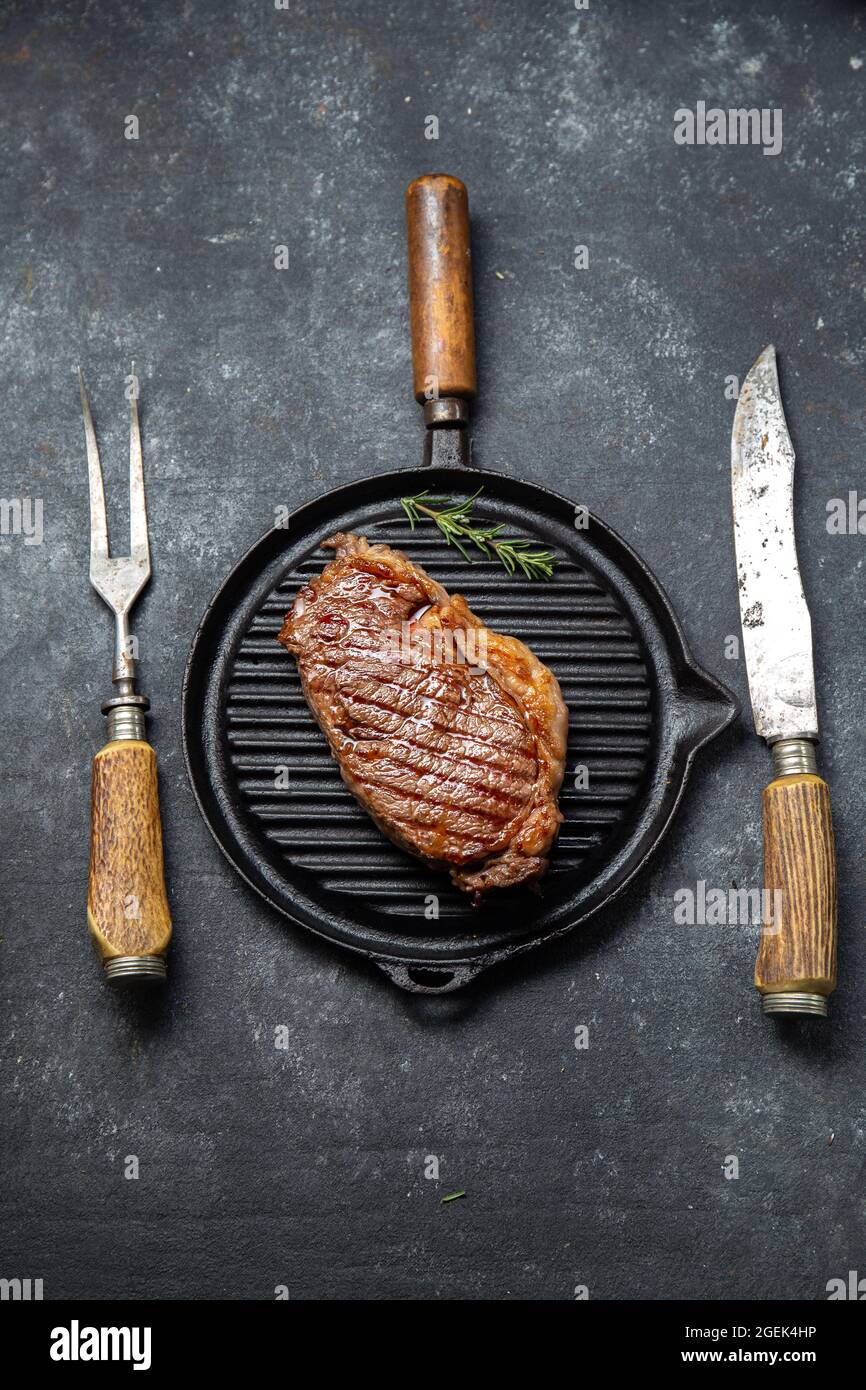 Fried strip loin steak on vintage cast iron grill pan and cutlery set