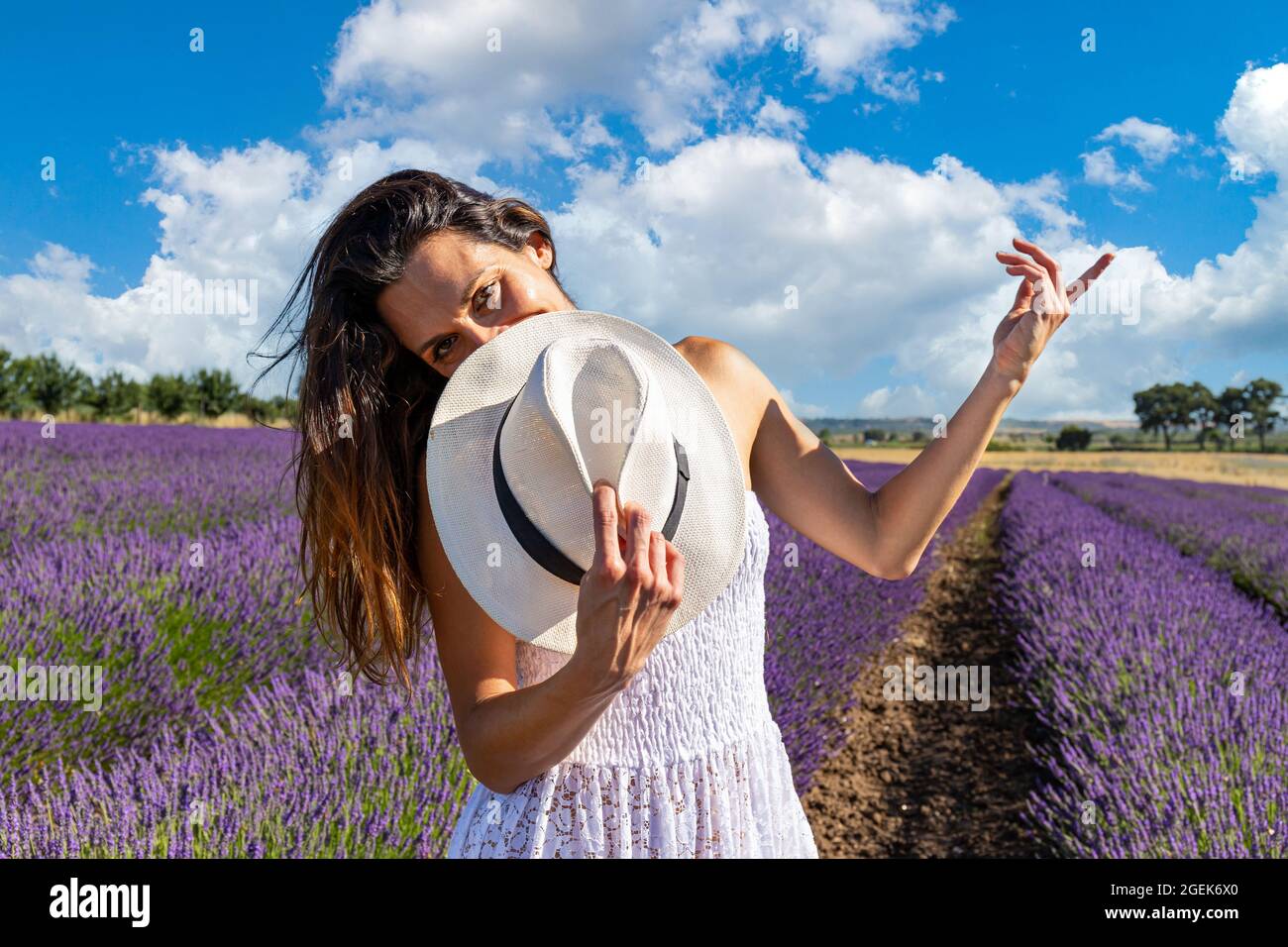 Happy young woman playing with her hat in a blooming lavender field. She has an intense gaze and eyes turned to the camera. Stock Photo