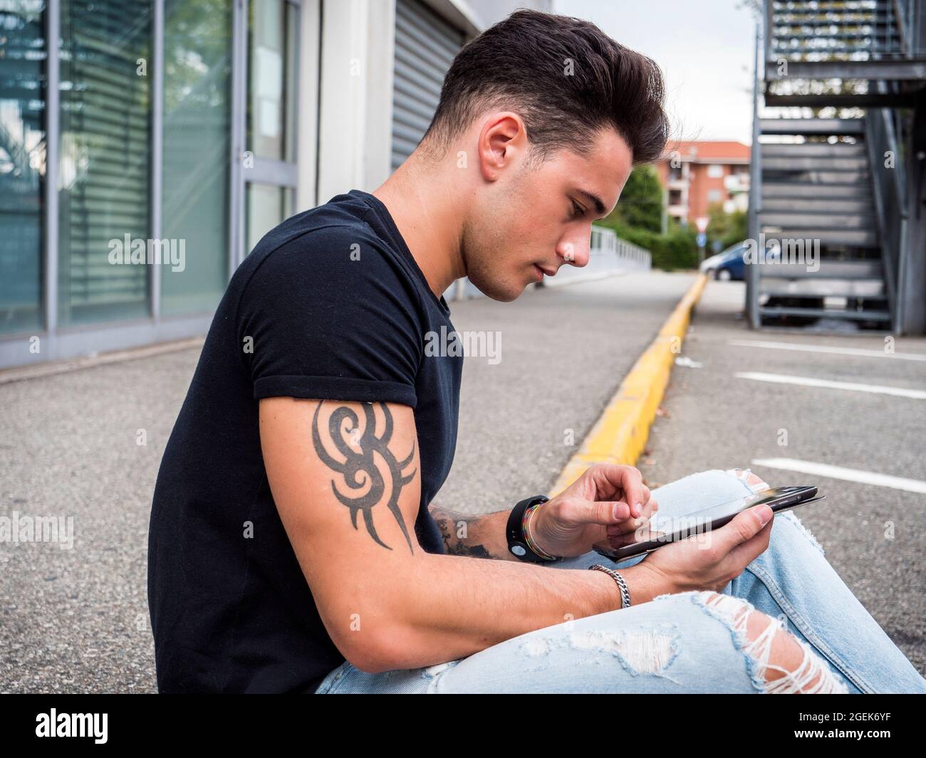 Young man using tablet PC sitting on street curb Stock Photo