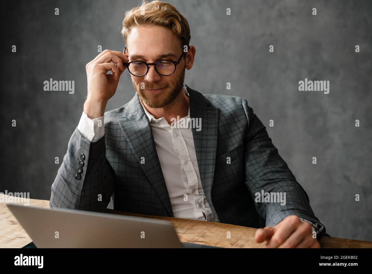 The smiling man straightening glasses and looking into laptop