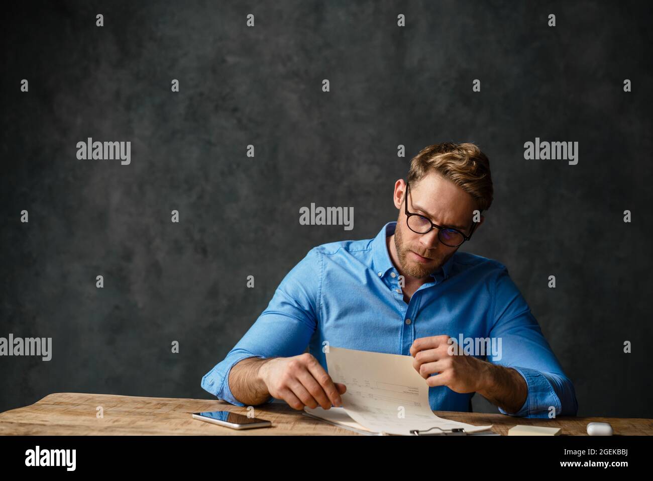 Frowning business man working with documents while sitting at the desk isolated over black background Stock Photo