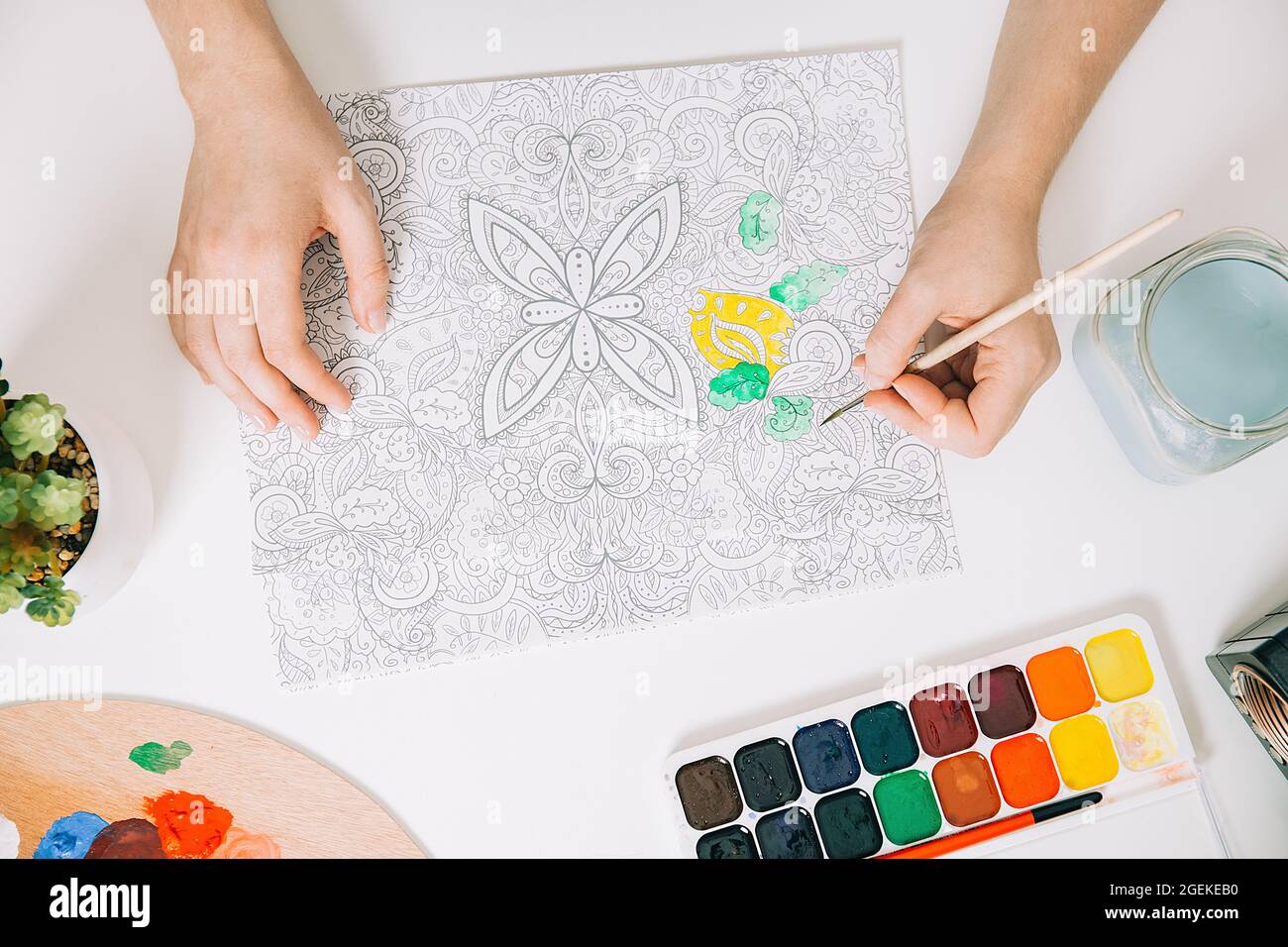 Art therapy or self expression for adults. Young woman is coloring page anti stress book, mental wellbeing concept. Workspace of artist - paints, penc Stock Photo