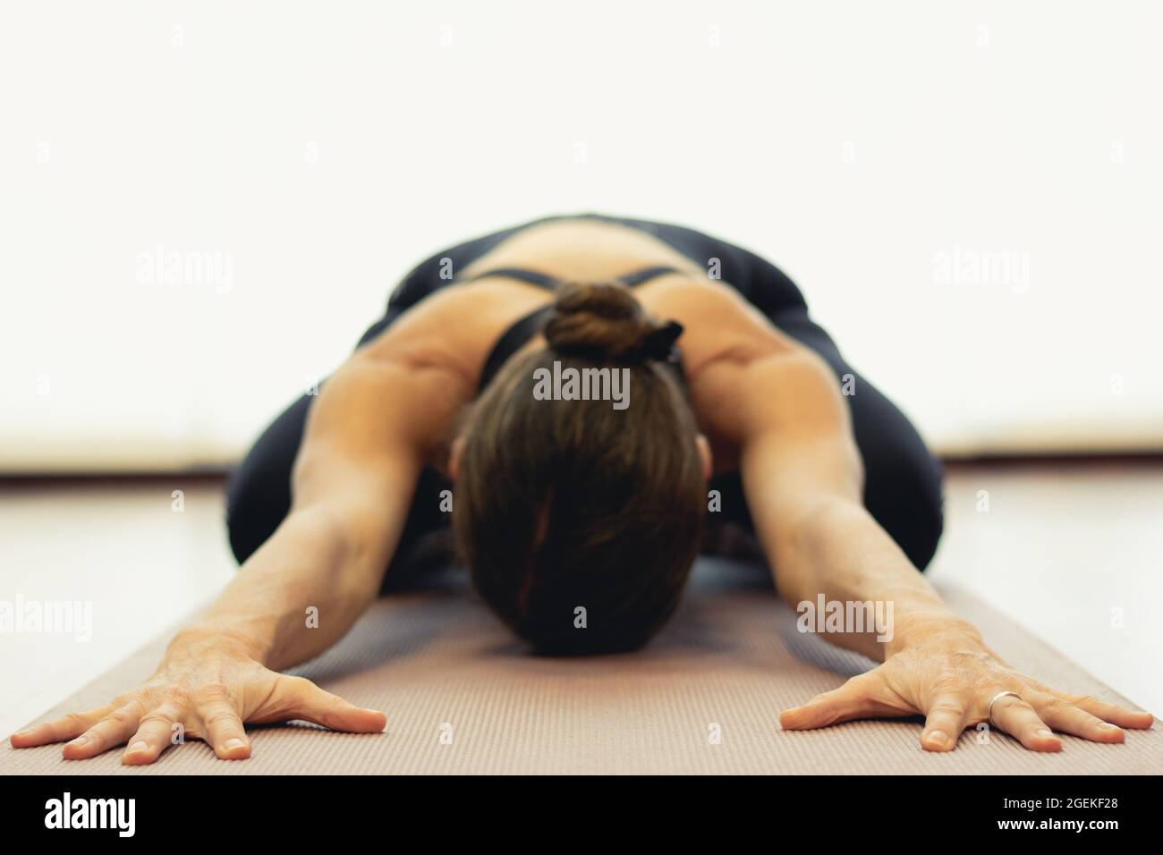 Yogi woman practices child pose in bright studio. Focus on hands of lady in balasana on pink mat. Healthy lifestyle, resting exercise, workout, sports Stock Photo