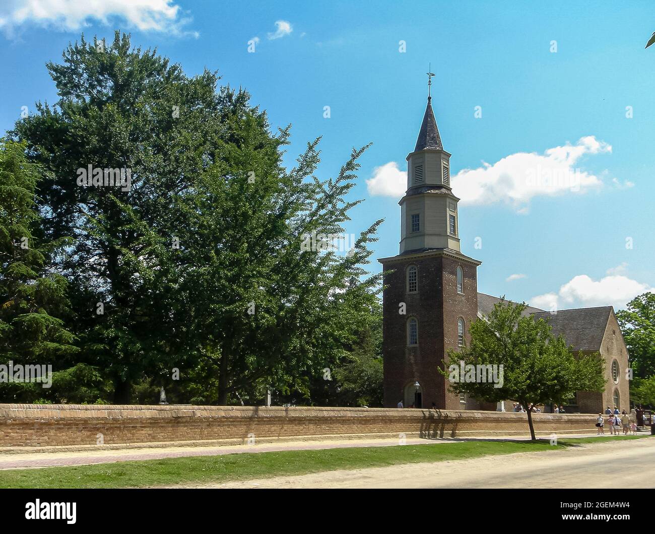 Williamsburg, VA, USA - June 20, 2006: Historic site. Bruton Episcopal parish church with set in its park against blue cloudscape. Visitors in street. Stock Photo