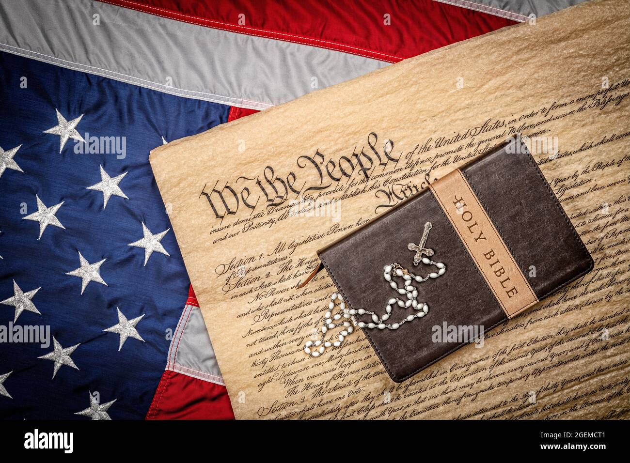 A holy bible and crucifix rest atop the United States Constitution and American flag, which is emblematic of freedom of religion without persecution. Stock Photo