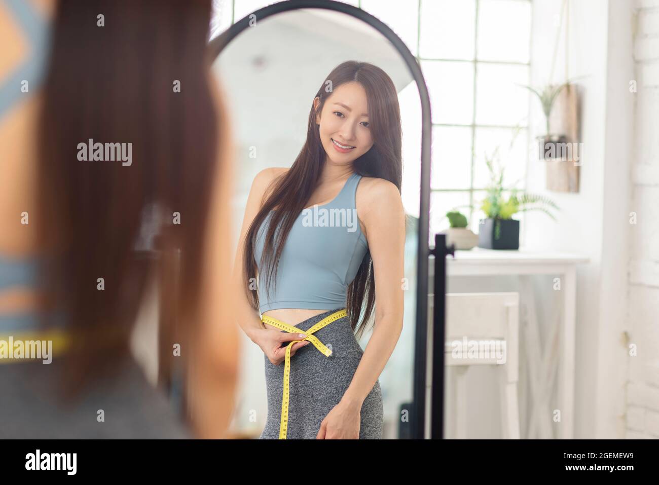 Young woman measuring waist with tape  and standing in front of mirror. Weight lossconcept Stock Photo