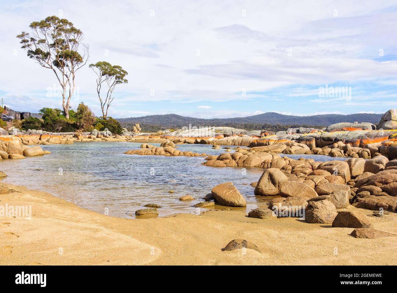 Little pond in Skeleton Bay surrounded by boulders draped in orange lichen - Binalong Bay, Tasmania, Australia Stock Photo