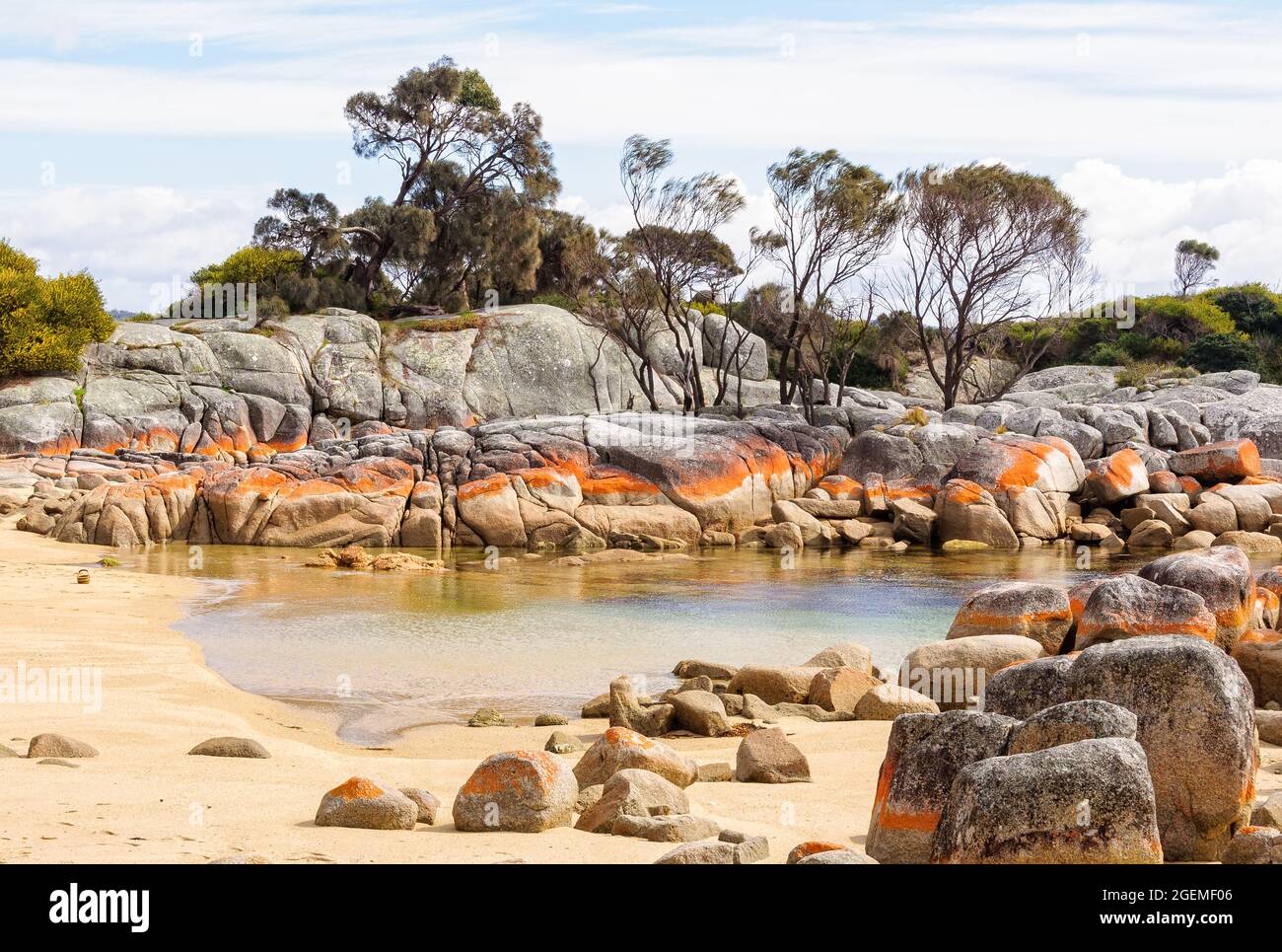 Little pond in Skeleton Bay surrounded by boulders draped in orange lichen - Binalong Bay, Tasmania, Australia Stock Photo