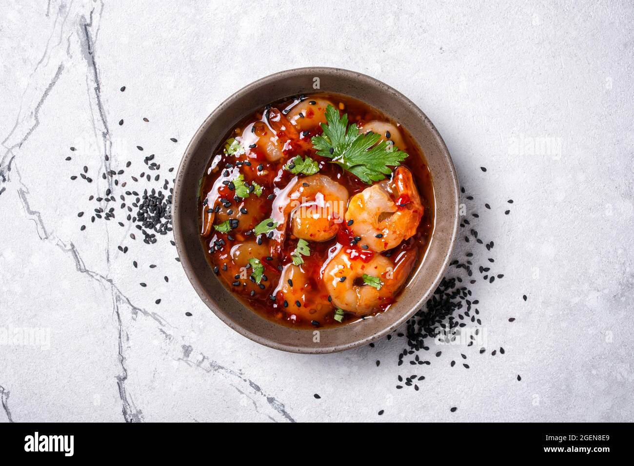 Top view of bowl with spicy shrimps in sweet chili asian sauce with black sesame seeds on white marble background Stock Photo