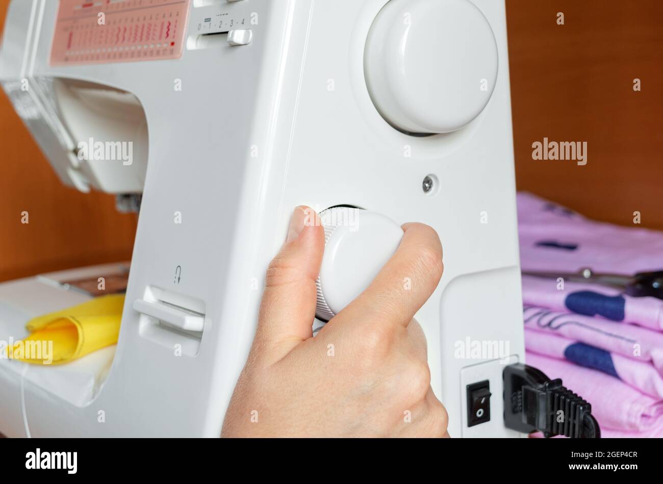 The hand turns the wheel of the sewing machine to adjust the stitch type, close-up. Stock Photo
