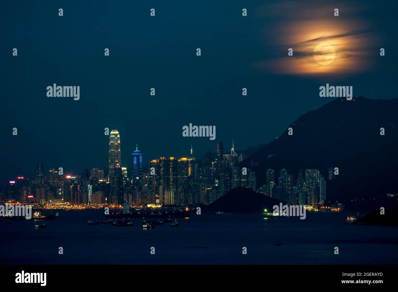 The full moon rises from behind Victoria Peak and the skyline of ...