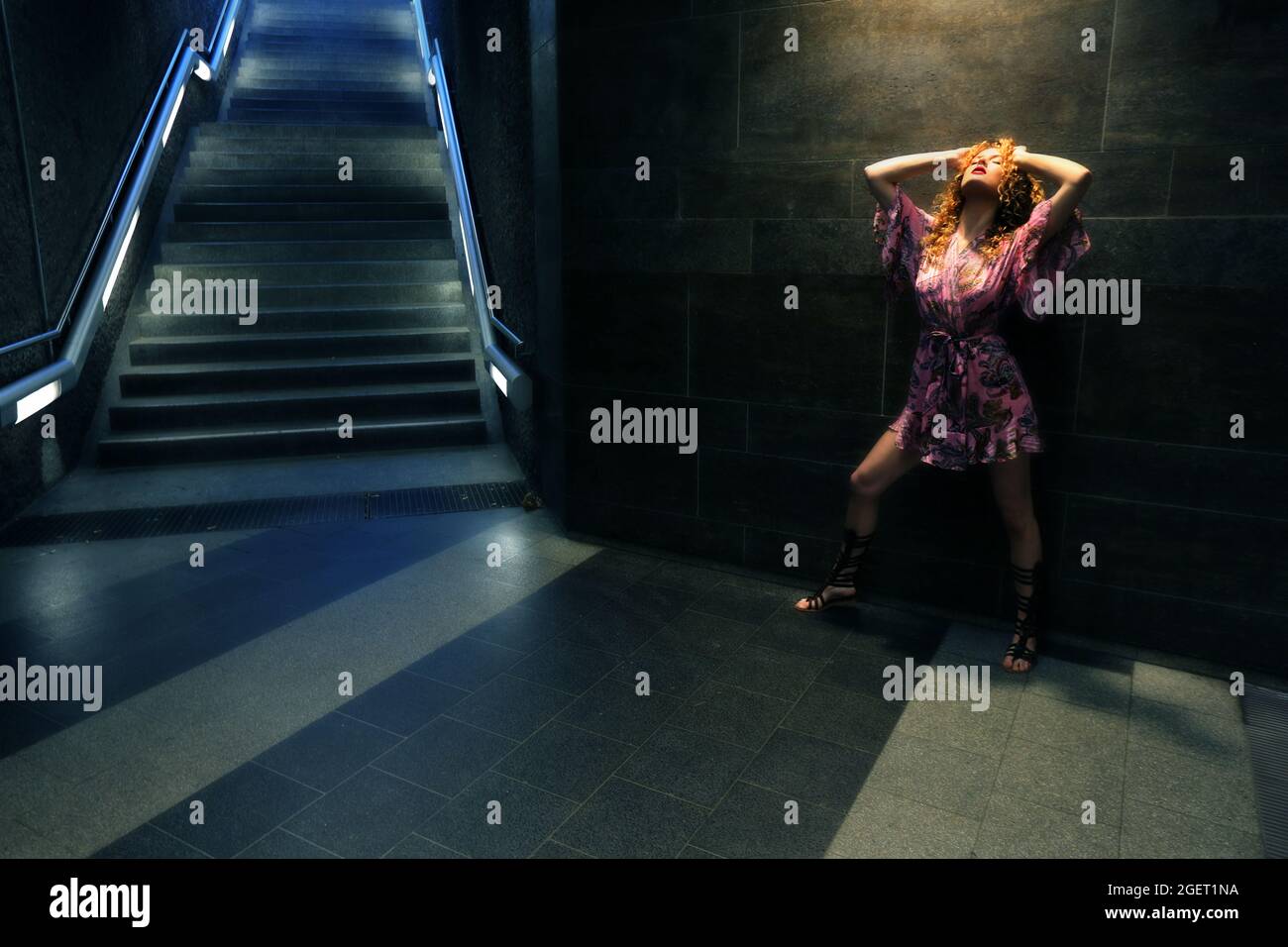U Bahnhof in Nürnberg, in der U Bahn oder Metro  steht eine rothaarige junge Frau mit pinken Kleid auf den Treppen zur Untergrundbahn Stock Photo