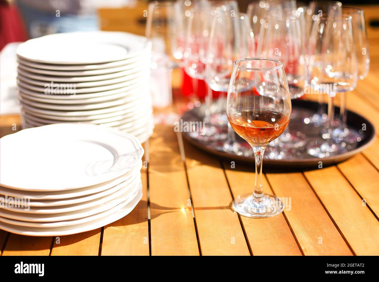 https://c8.alamy.com/comp/2GETAT2/wooden-table-with-lots-of-clean-white-plates-and-wine-glasses-on-round-tray-in-outdoor-restaurant-on-sunny-day-set-of-tableware-and-glassware-select-2GETAT2.jpg