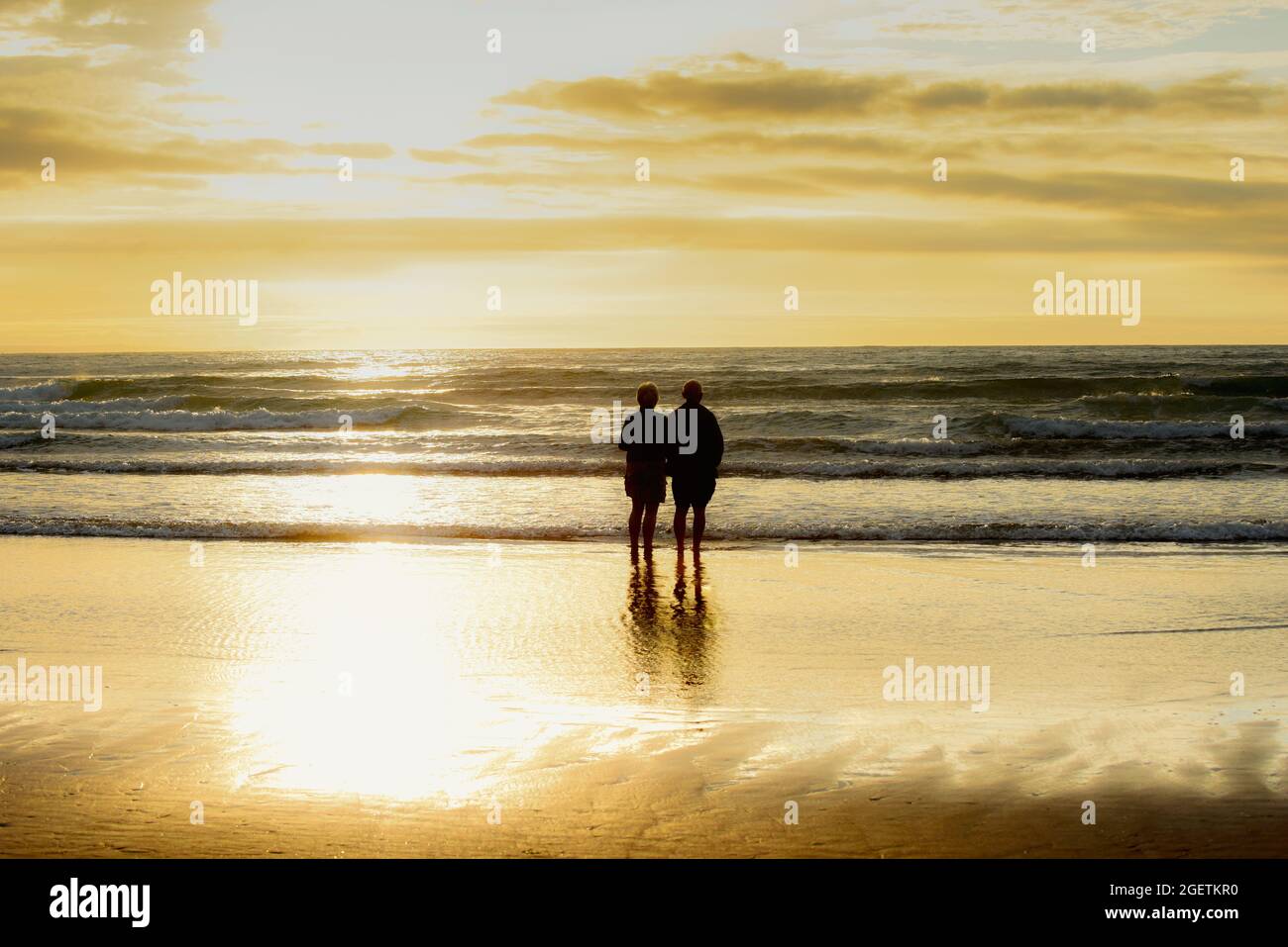 Romantic senior couple of retirement age looking out to sea at sunset Stock Photo