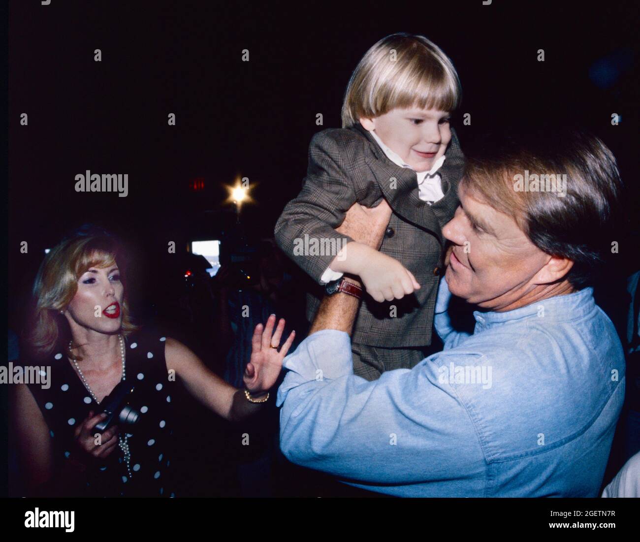 Glen Campbell lifts up one of the many young grandchildren, children, nieces and nephews who were part of his 60th birthday celebration on April 20th, 1996 in Branson, Missouri. The event was held two days before his actual birthday on April 22. Campbell's wife, Kim is at left. Stock Photo