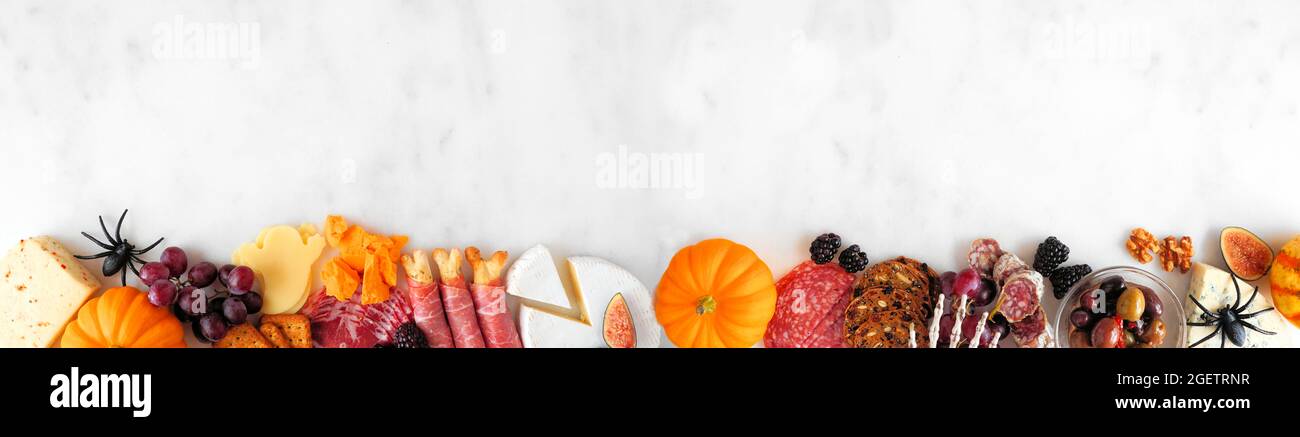Halloween charcuterie border against a white marble banner background. Selection of cheese and meat appetizers. Copy space. Stock Photo