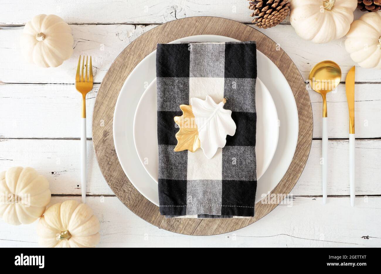 Autumn harvest or thanksgiving dinner table setting with plates, flatware, buffalo plaid napkin, pumpkins and decor. Top view on a white wood backgrou Stock Photo