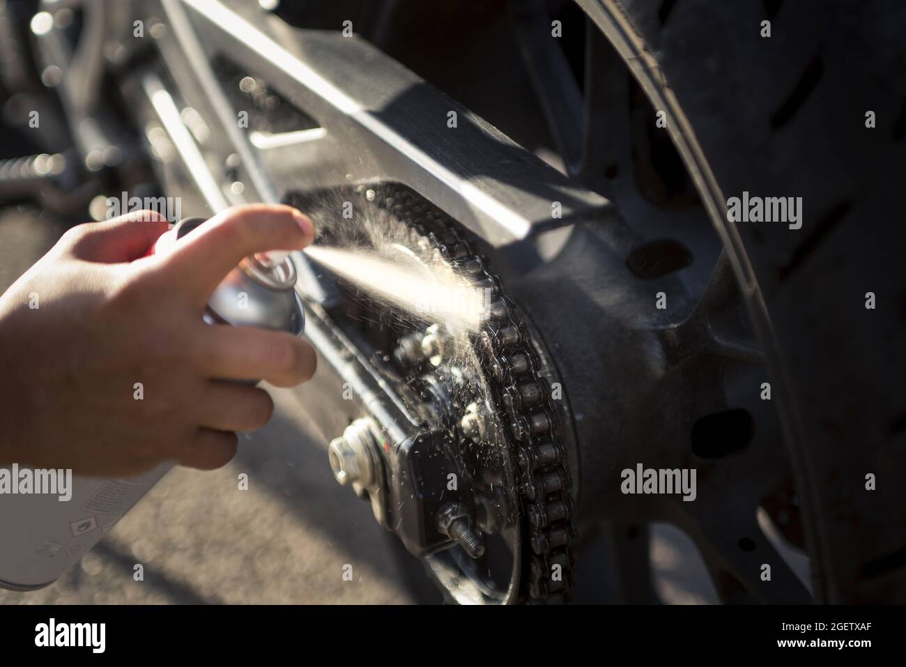 Closeup of a person oiling the chain of a modern motorcycle with a ...