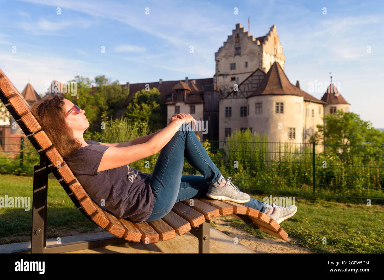 Young woman rests at Meersburg Castle, Germany. This place is tourist attraction of Lake Constance. Adult girl sunbathes near Swabian landmark at suns Stock Photo