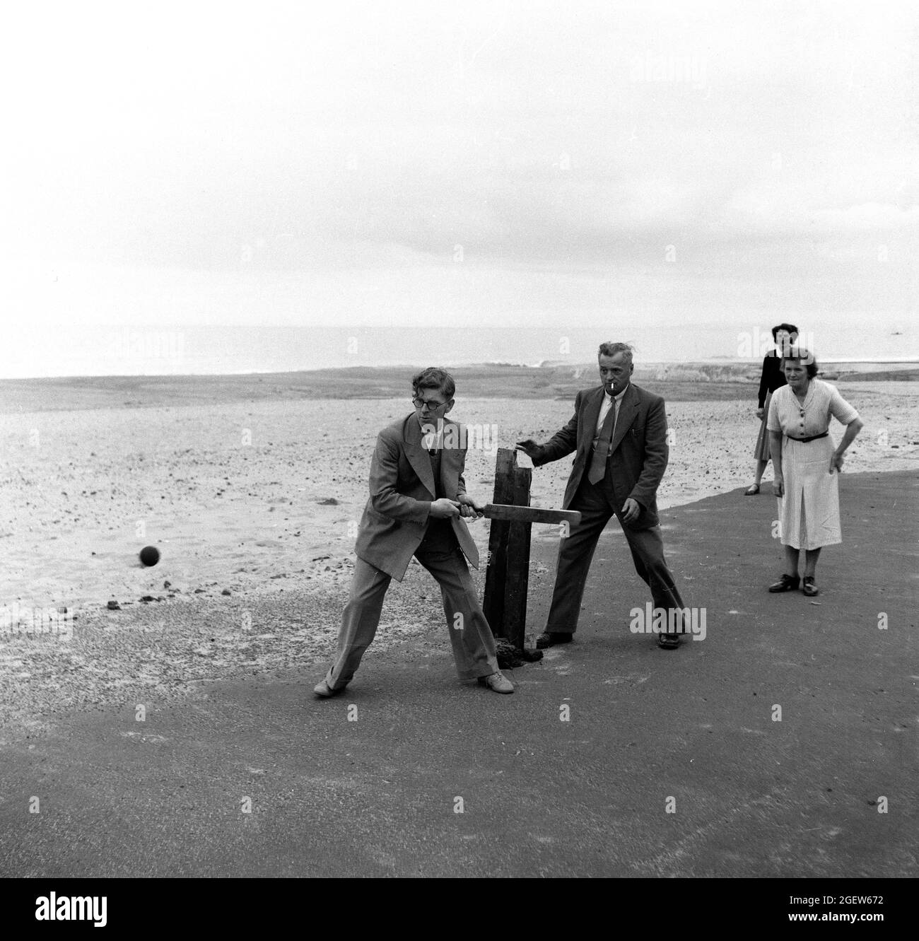 Family playing makeshift cricket at the seaside Britain 1950s Stock Photo