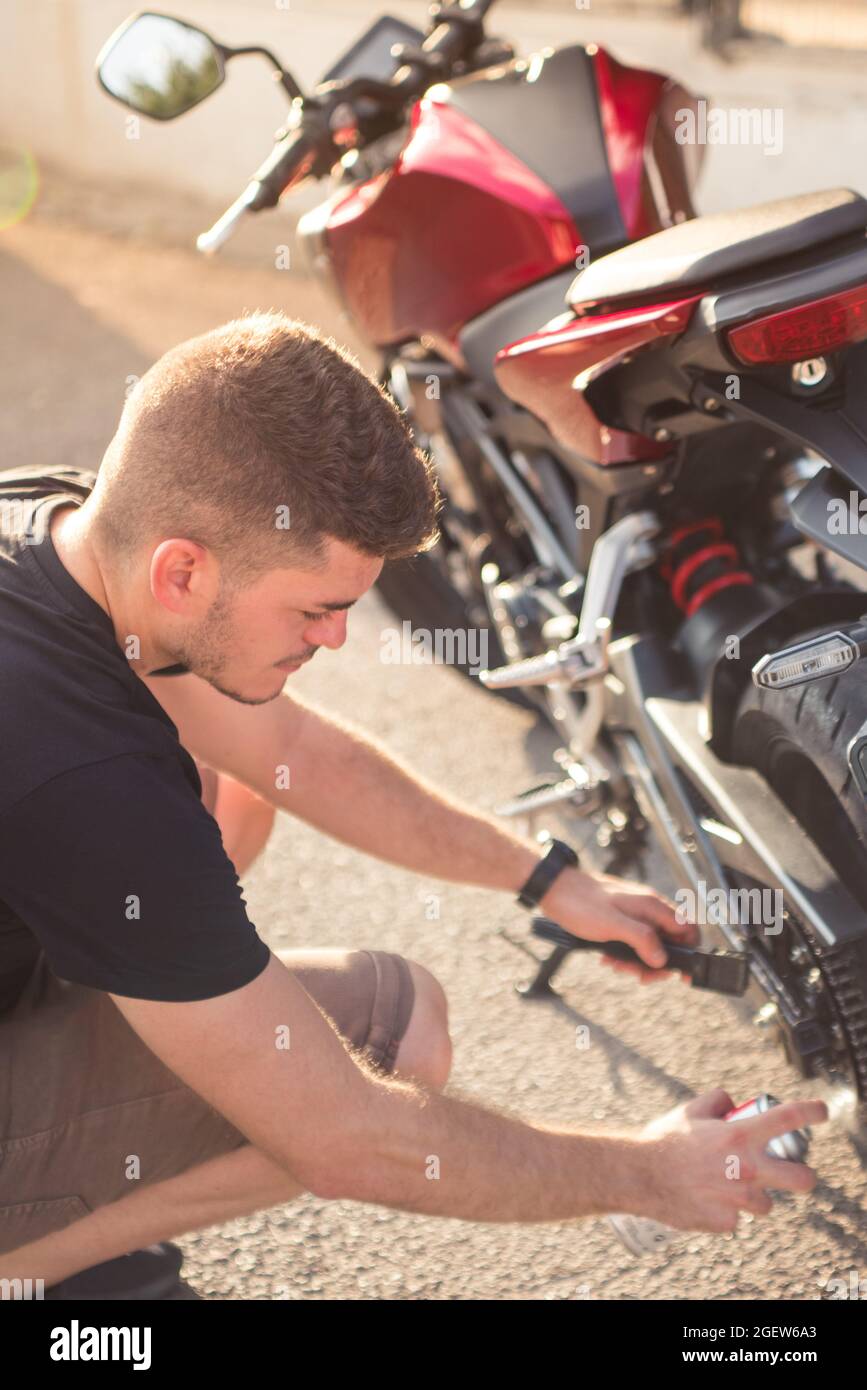 Adult man oiling the chain of a modern motorcycle with a spray can outdoors Stock Photo Alamy