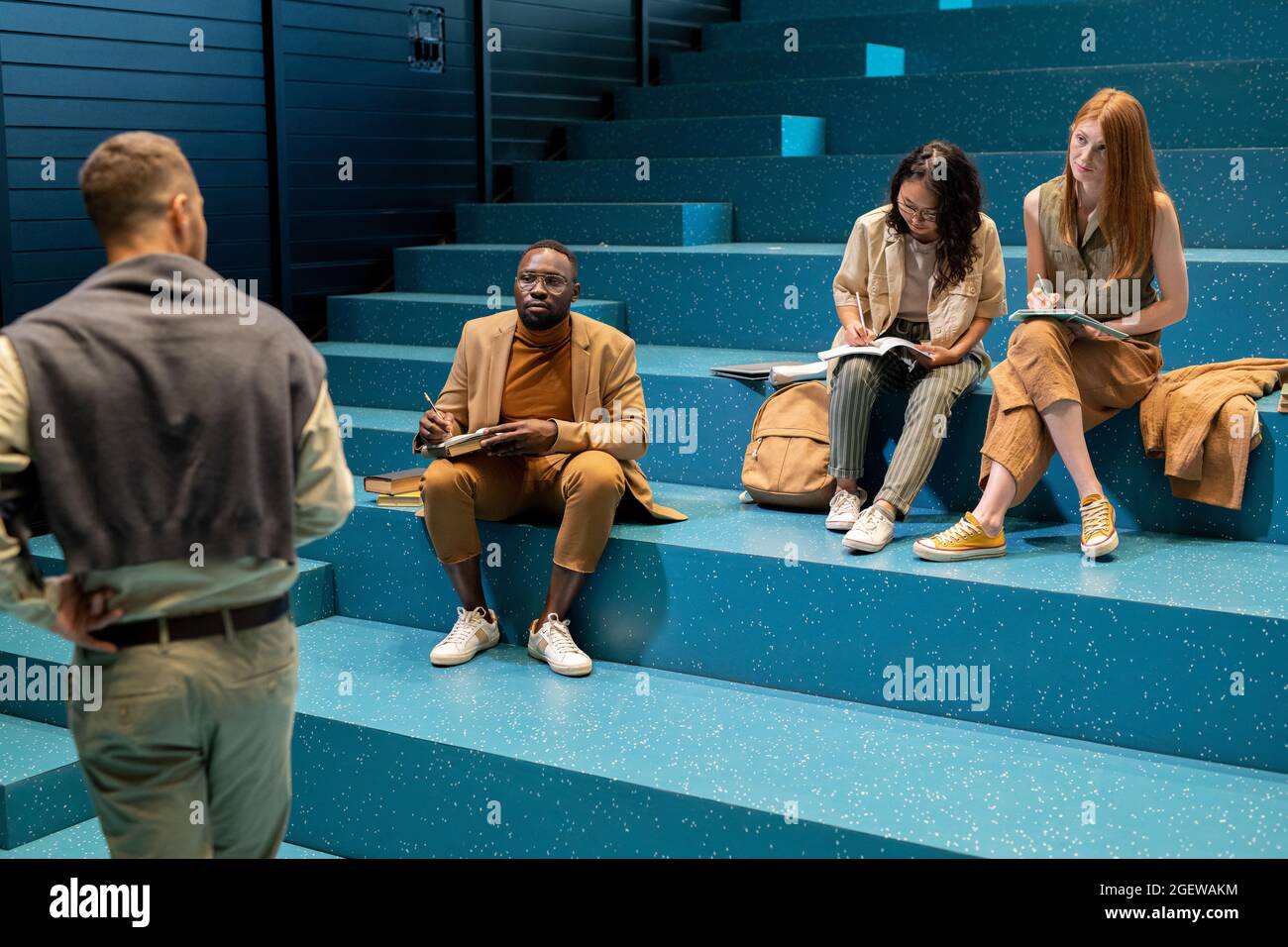 Diligent students in smart casualwear looking at coach and making notes at lecture Stock Photo