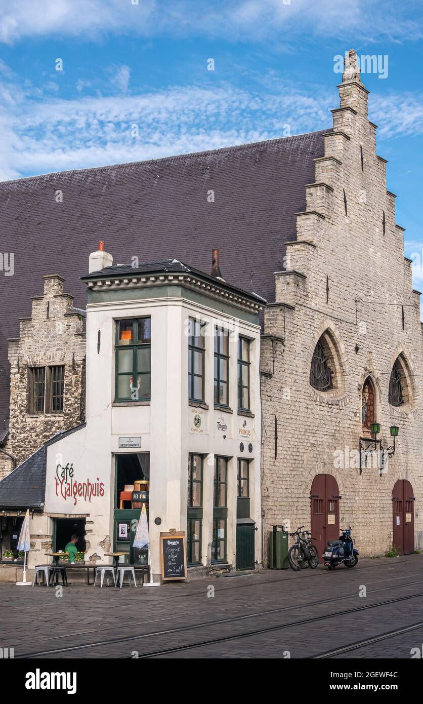 Gent, Flanders, Belgium - July 30, 2021: White small Gelgenhuis pub adjacent to historic  beige brick and dark roof medieval meat market building unde Stock Photo