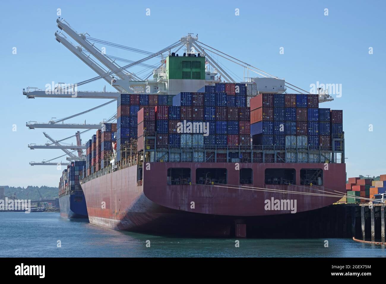 Two large container ships are shown dock in a port next to industrial cranes. Stock Photo