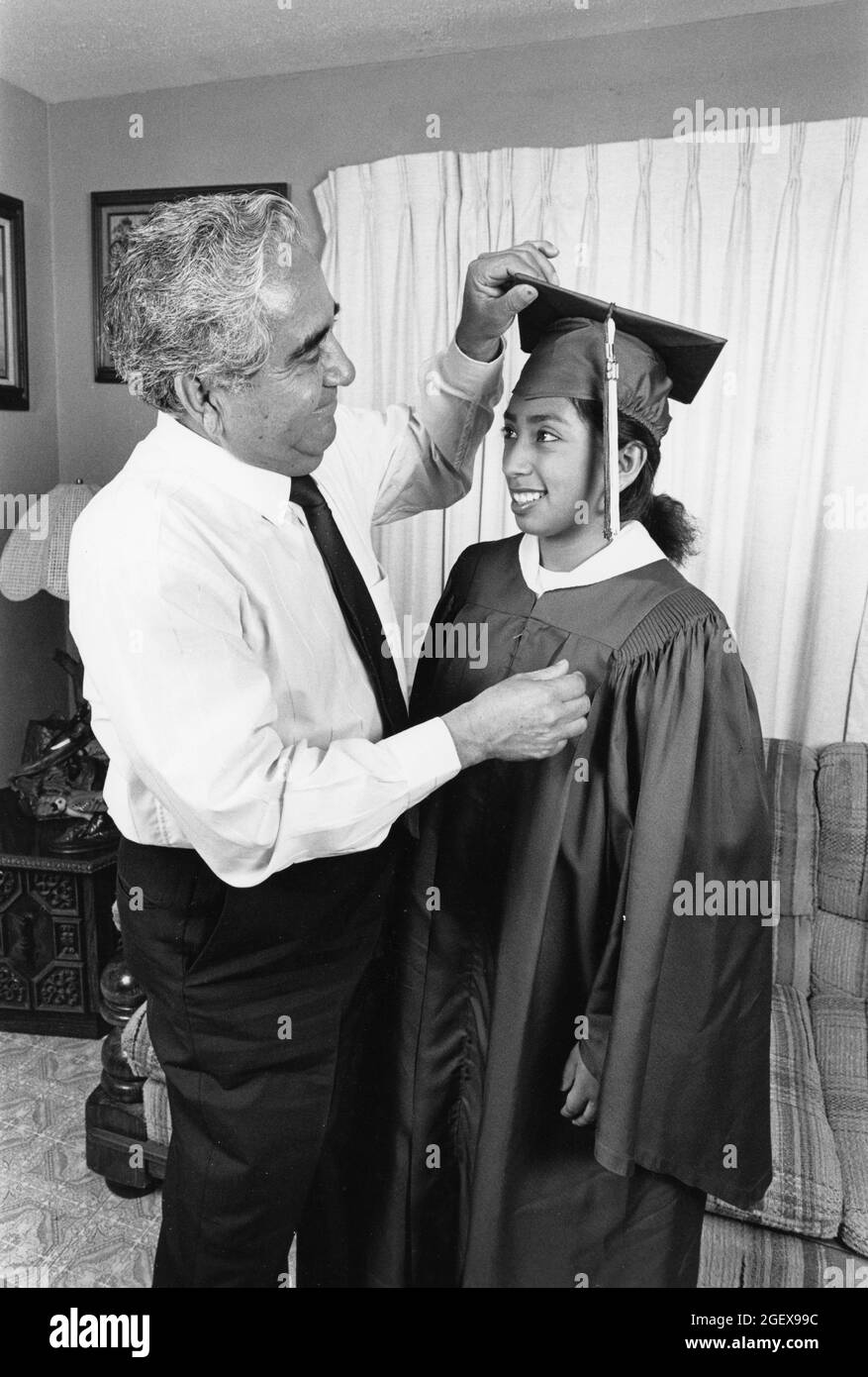 San Antonio Texas USA, circa 1990: Proud father adjusts daughter's mortarboard at home before her commencement ceremony from Edgewood High School. Her father, Demetrio Rodriguez, is the named plaintiff in Rodriguez v. San Antonio Independent School District, which led to the landmark Edgewood v. Kirby lawsuit that forced the state of Texas to make its funding of public schools more equitable between districts serving rich and white students and those serving poor and minority students.  MR ES-0122 Model Released  ©Bob Daemmrich Stock Photo