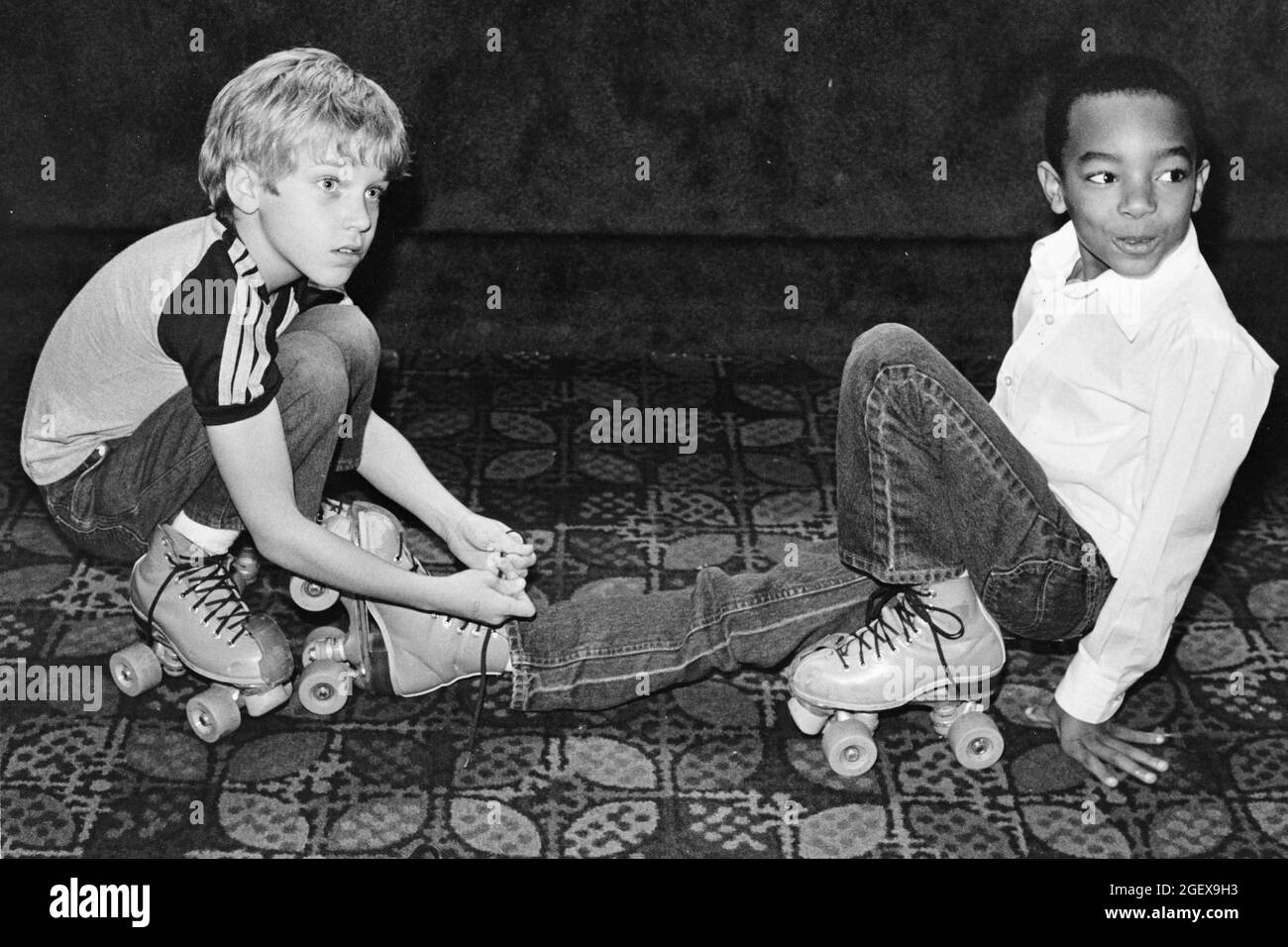 Luling Texas USA, circa 1988: Young white boy ties laces of his Black friend's skating boot at roller rink. ©Bob Daemmrich Stock Photo