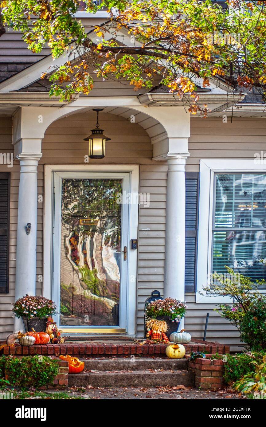 Traditional house with porch decorated for fall with partly eaten pumpkins and a squirrel eating another one - distorted reflections in storm window - Stock Photo